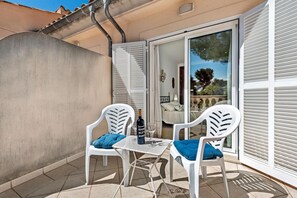 Une petite terrasse extérieure avec deux chaises en plastique blanc, une table et une bouteille de vin.
