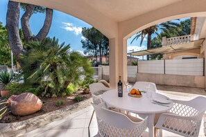 Une terrasse extérieure avec une table ronde, des chaises blanches, une bouteille de vin et une assiette de fruits.
