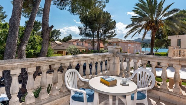 A balcony with a table and chairs, overlooking a scenic view of houses and a body of water.