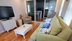 Ein Wohnzimmer mit einem grünen Sofa, einem weißen Couchtisch, einem grauen Sessel und einem Flachbildfernseher auf einem weißen Schrank.