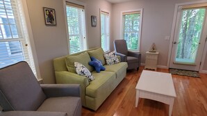 Ein Wohnzimmer mit einem grünen Sofa, einem grauen Sessel, einem weißen Couchtisch und einem Deckenventilator.