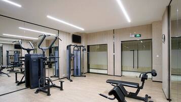 Un gimnasio moderno con diversas máquinas de ejercicio, una banca y un espejo.
