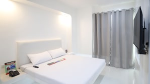 Ett modernt hotellrum med en stor säng, en platt-TV och ett nattduksbord med en telefon och en tidning.
