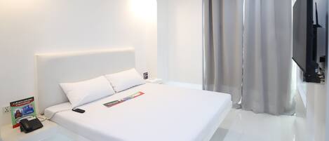 A modern hotel room with a large bed, a flat-screen TV, and a bedside table with a phone and a magazine.
