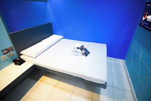 Una habitación de hotel con una cama, una mesita de noche, un teléfono y un televisor de pared.