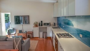 Cocina compacta con gabinetes blancos, microondas, estufa a gas y un lavamanos. Hay un pequeño comedor con mesa y sillas, y un televisor montado en la pared.