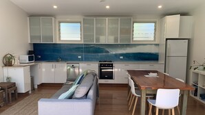 Una cocina moderna con armarios blancos, un protector de salpicaduras azul, una mesa de comedor con sillas y un sofá.