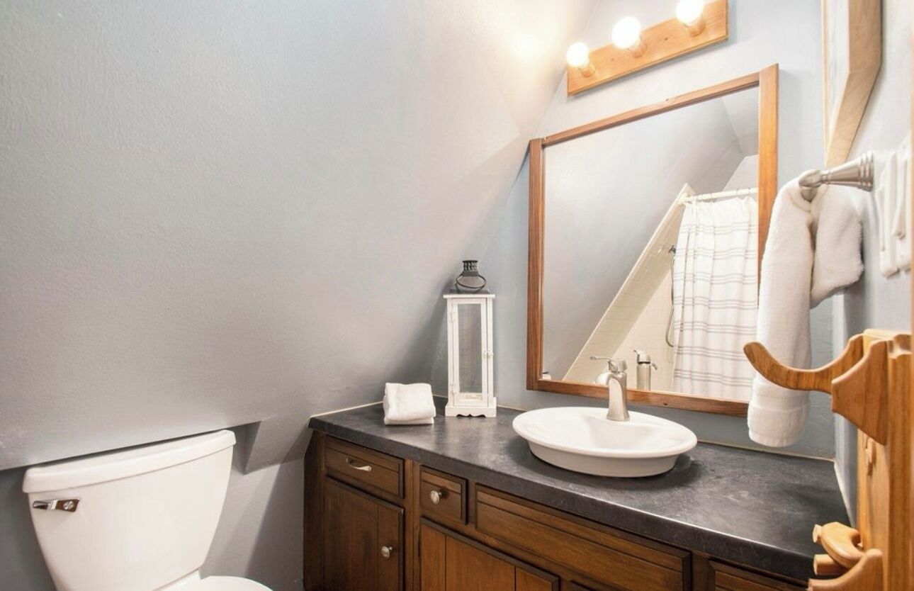 Un baño con inodoro blanco, tocador de madera con lavamanos, espejo y toallero.
