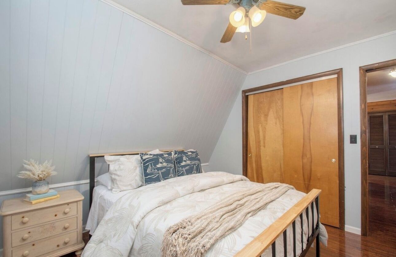 A bedroom with a bed, a wooden door, a dresser, and a ceiling fan.