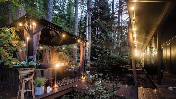A wooden deck with string lights, a seating area with cushions, and potted plants.