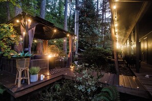 Une terrasse en bois décorée de guirlandes lumineuses, un coin salon avec des coussins et des plantes en pot.
