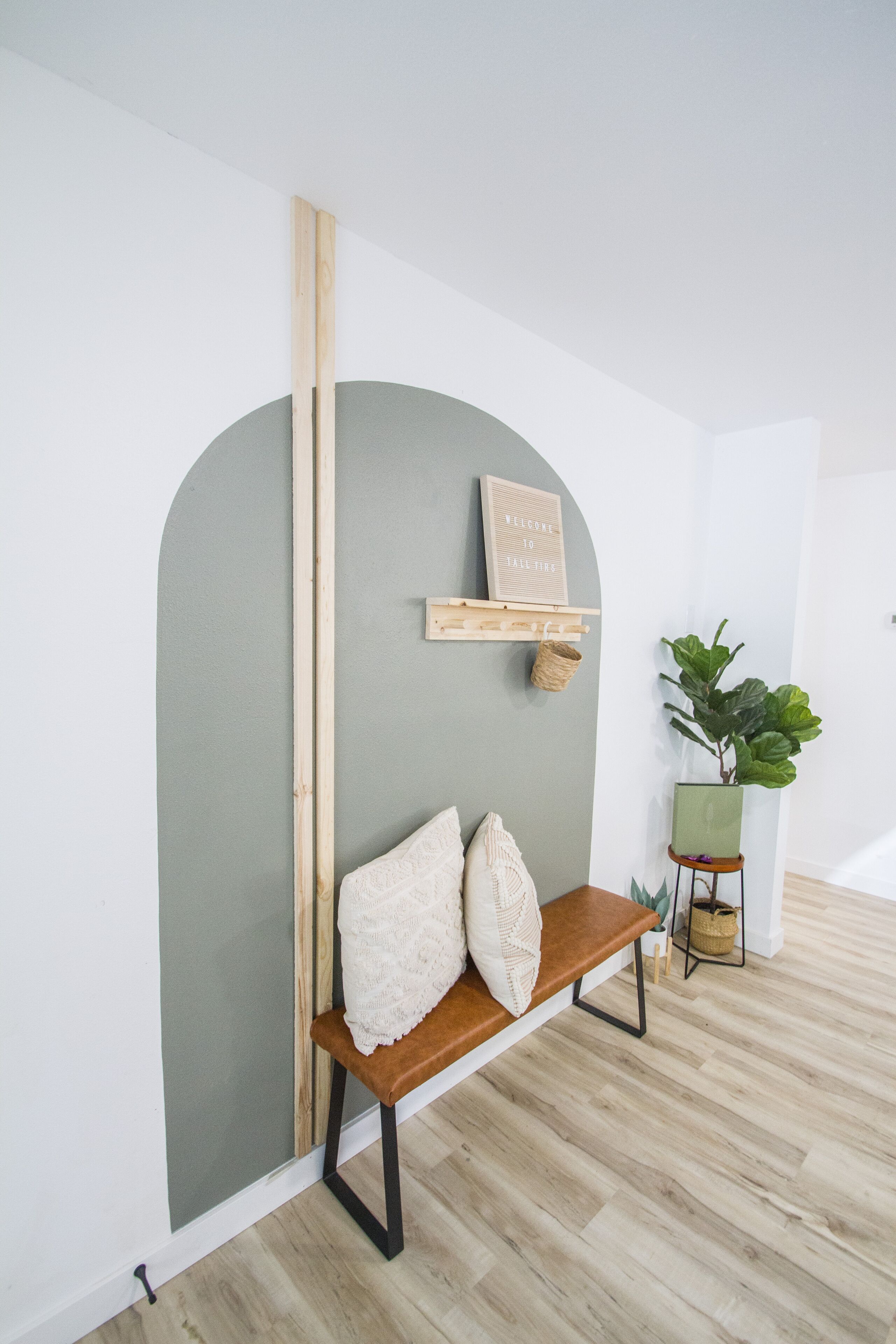 A room with a wooden bench, a green plant, and a wall-mounted shelf with a welcome sign.
