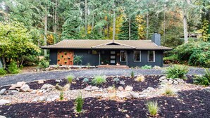 A house surrounded by a forest with a gravel driveway and a well-maintained garden.
