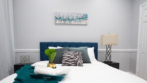 Ein ordentlich eingerichtetes Schlafzimmer mit Bett, Kissen, Nachttisch, Lampe und einem Wandbild.