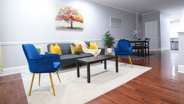 Ein Wohnzimmer mit einer Couch, zwei blauen Sesseln, einem Couchtisch und einem Gemälde an der Wand.