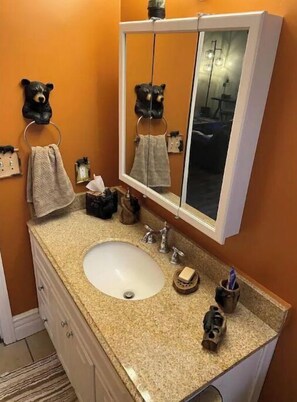 Sink, mirror, and granite countertop in a bathroom with towel rings and toiletries.