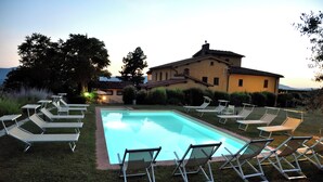 A swimming pool with lounge chairs and a large building in the background. - Il Bellini - Farmholiday Apartment Orciaia (Castelfranco Piandisco)