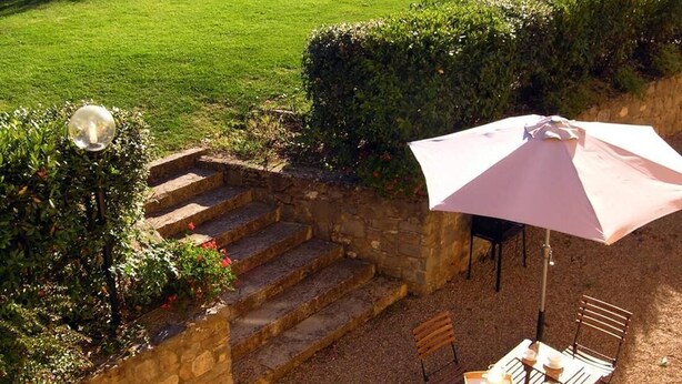 A patio area with a table and chairs, a pink umbrella, and a stone staircase leading to a grassy area with lounge chairs. - Il Bellini - Farmholiday Apartment Orciaia (Castelfranco Piandisco)