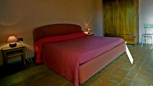 A bedroom with a large bed, a wooden wardrobe, a nightstand with a lamp, and a chair. - Il Bellini - Farmholiday Apartment Orciaia (Castelfranco Piandisco)