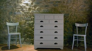 A stone wall with a white dresser and two white chairs. - Il Bellini - Farmholiday Apartment Orciaia (Castelfranco Piandisco)