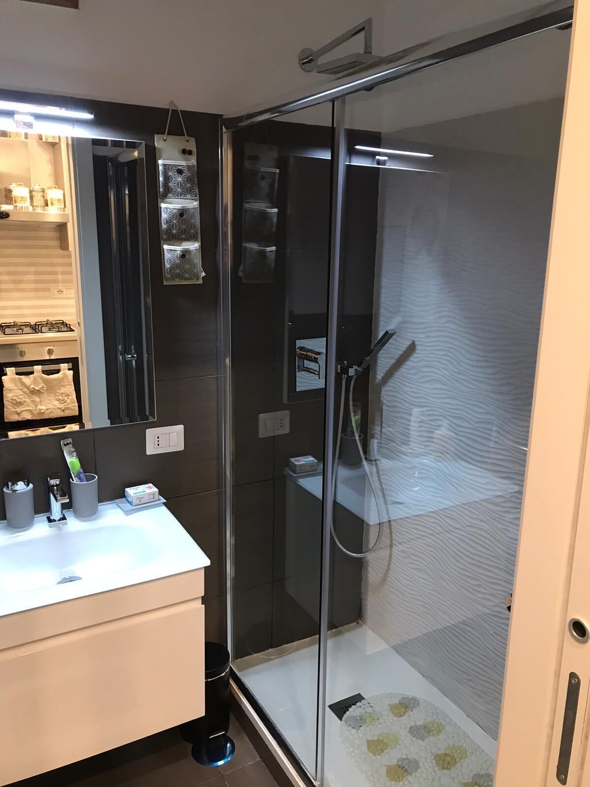 Une salle de bain moderne avec une douche à parois de verre, un lavabo blanc avec un miroir et un plan de toilette avec des articles de toilette.
