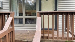 A wooden deck with a glass door marked "411" leading to a house with white siding and a window.