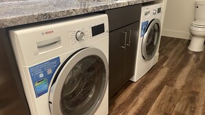 A modern kitchen with a Bosch washing machine and a Bosch dishwasher, a marble countertop, and a wooden floor.