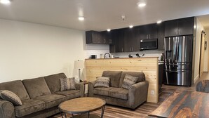 A modern kitchen with dark cabinets, a stainless steel refrigerator, and a wooden dining table.