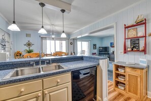 Una cocina con encimeras de granito, lavavajillas, armarios de madera, luces colgantes y un estante rojo con objetos decorativos.