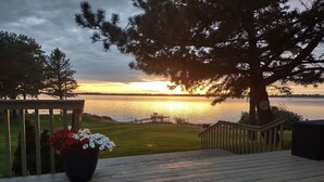 A wooden deck with a railing, a potted plant, and a view of a sunset over a body of water. - Lake Luxury home: Elegance,Comfort,Fishing,Hunting. (Watertown)