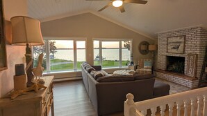 A cozy living room with a fireplace, a sofa, a lamp, and a view of the water. - Lake Luxury home: Elegance,Comfort,Fishing,Hunting. (Watertown)