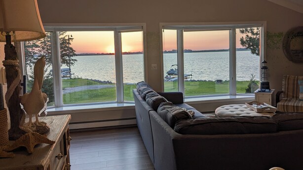 A living room with a large window overlooking a lake, a sofa, and a lamp. - Lake Luxury home: Elegance,Comfort,Fishing,Hunting. (Watertown)