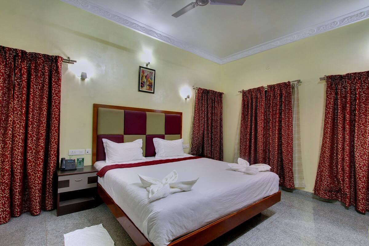 A hotel room with a bed, curtains, a bedside table, a phone, and a ceiling fan.