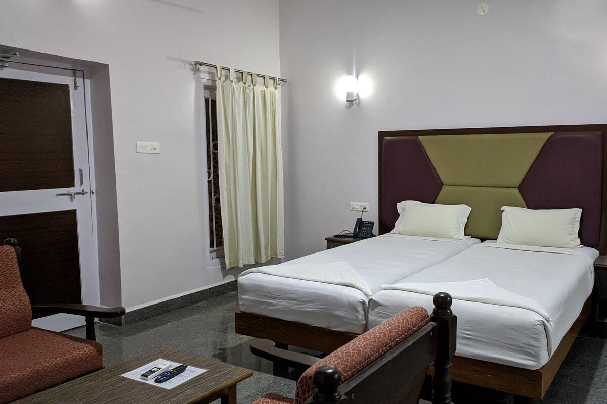 A hotel room with a double bed, a bedside table, a chair, a desk, a telephone, and a window with curtains.