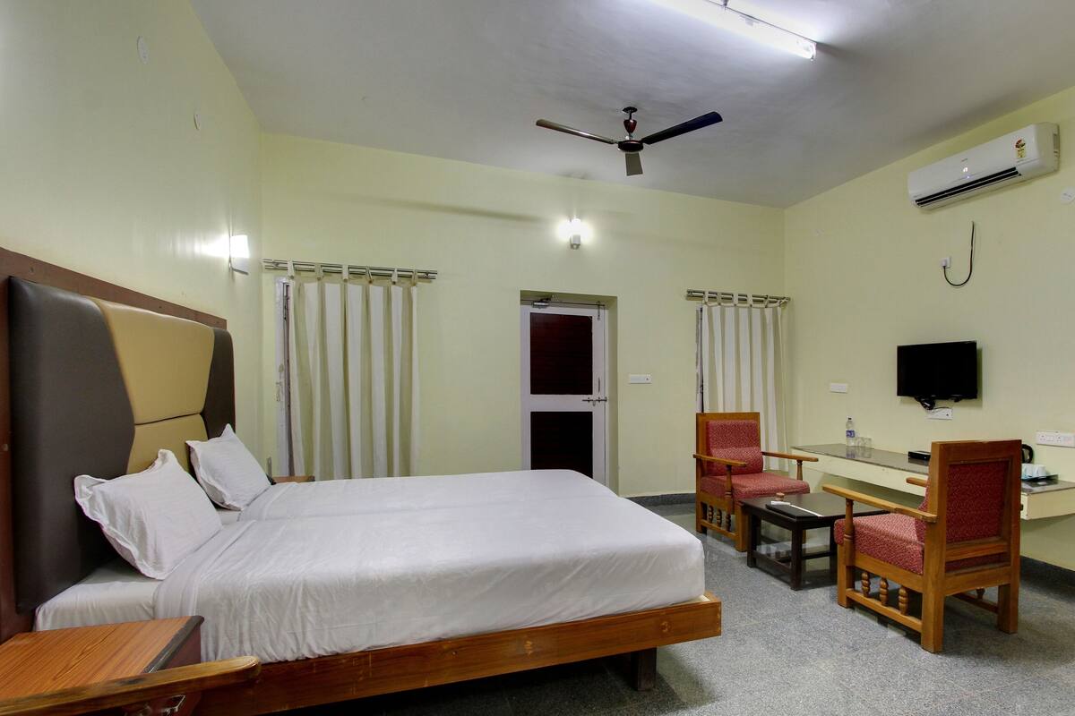 A hotel room with a bed, a desk, a chair, a television, and an air conditioning unit.