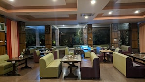 A restaurant with booths and tables, stone walls, and a view of trees outside. - Kanthi Resorts Badami (Bagalkot)