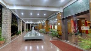 A hotel lobby with a central water feature, stone pillars, and potted plants. - Kanthi Resorts Badami (Bagalkot)