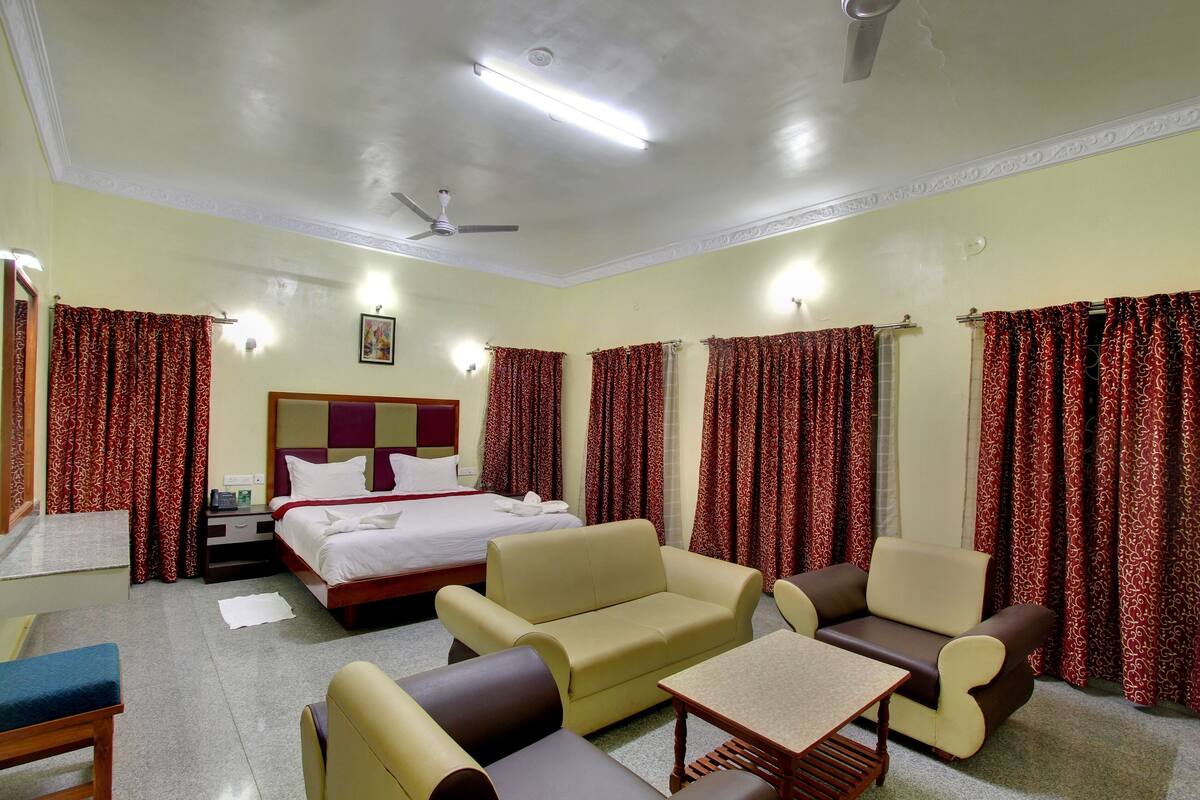 A hotel room with a bed, sofa, armchair, table, and curtains.