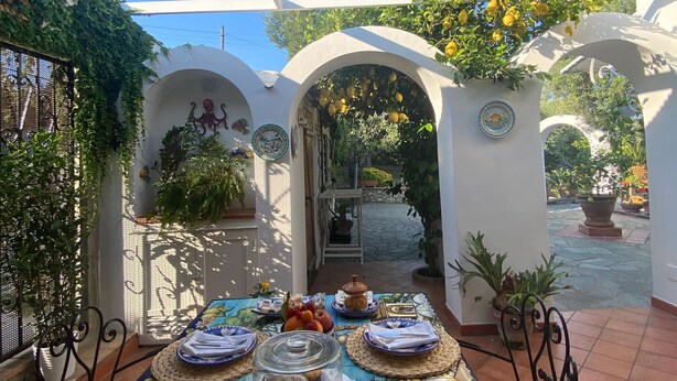 An outdoor patio with a table set for breakfast, surrounded by white arches and potted plants. - Room-the Archi B&B Apartment (Anacapri)