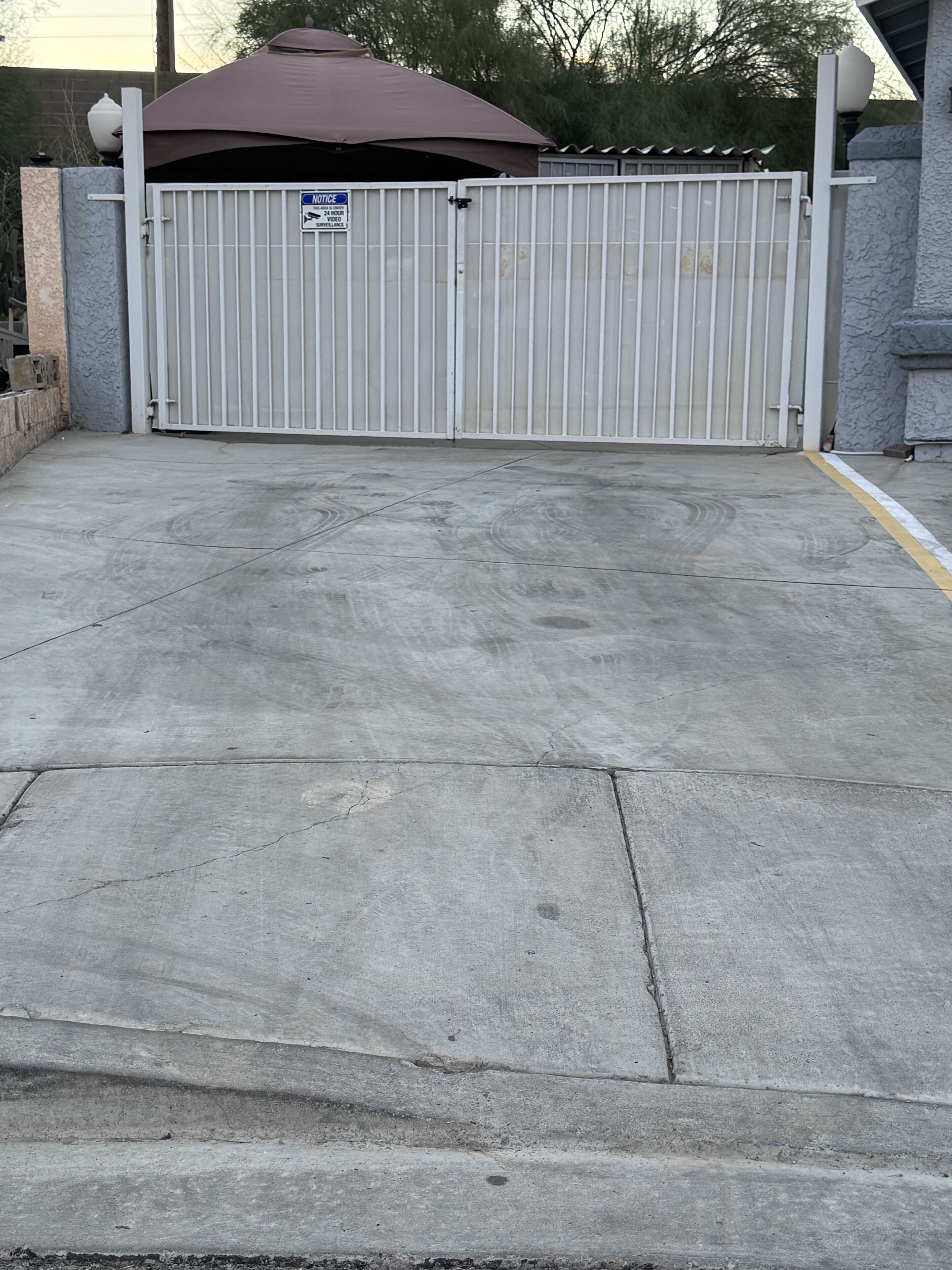 A gated parking area with a concrete surface, a notice sign, and a brown awning.