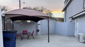 A backyard patio with a table and chairs under a canopy, a trash bin, and a fence. - Beautiful suited with separate entrance (Las Vegas)