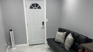 A room with a white door, a black leather sofa with patterned cushions, a small table, and a standing heater. - Beautiful suited with separate entrance (Las Vegas)