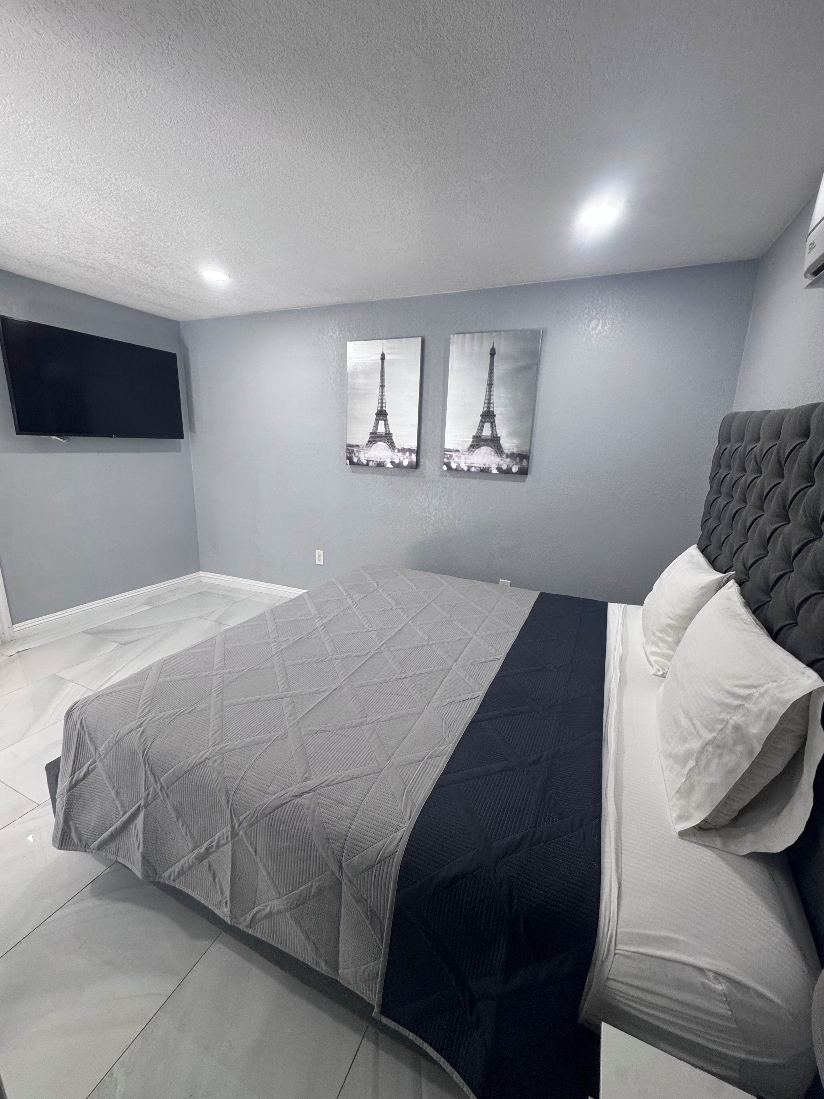 Une chambre moderne avec un grand lit, un téléviseur à écran plat fixé au mur et deux tableaux représentant la Tour Eiffel.