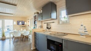 Une cuisine moderne avec des armoires grises, un plan de travail en bois et un four encastré. On aperçoit à l’arrière-plan un coin repas avec une table et des chaises.