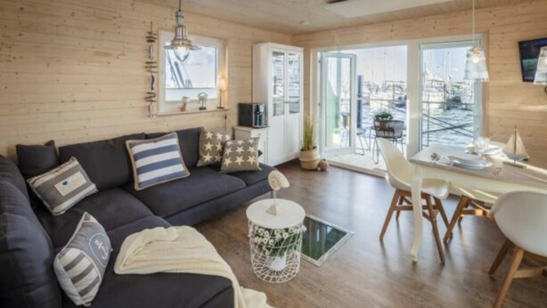 Un salon moderne avec un canapé foncé, une petite table d’appoint ronde blanche et un coin repas comprenant une table et des chaises blanches.