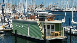 Une péniche flottante est amarrée dans une marina, entourée de plusieurs autres bateaux.