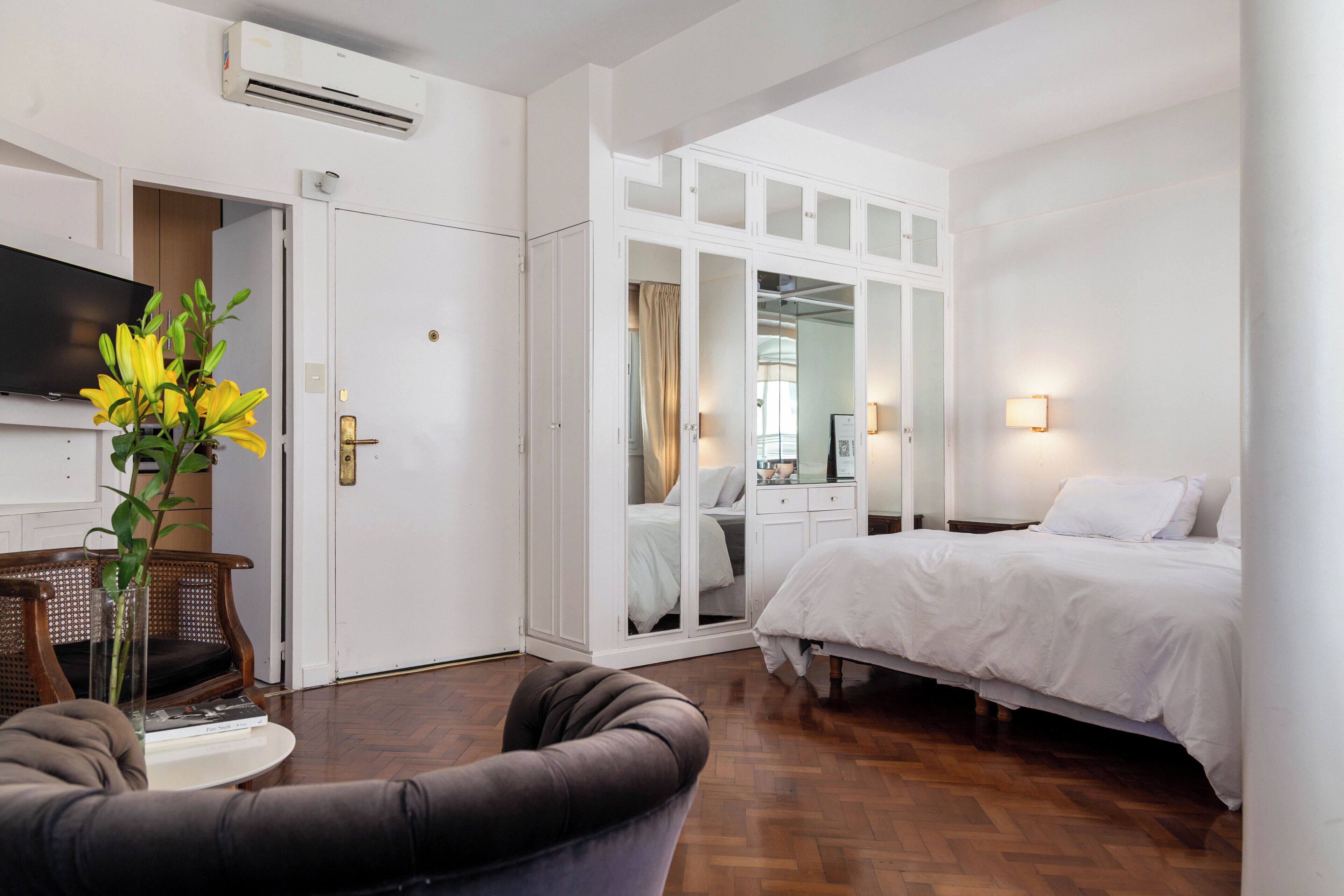 A hotel room with a bed, a TV, a wardrobe, and a seating area with a plant.