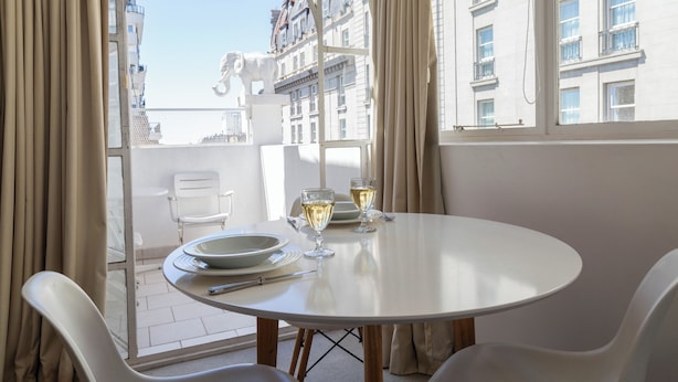 A round table with white chairs, two glasses of white wine, and a plate on a balcony overlooking a cityscape. - BT Homes - Recoleta, Ayacucho (Buenos Aires)