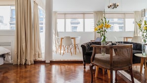 A spacious living room with a wooden herringbone floor, a dark leather sofa, a wooden coffee table, and a large window with curtains. - BT Homes - Recoleta, Ayacucho (Buenos Aires)