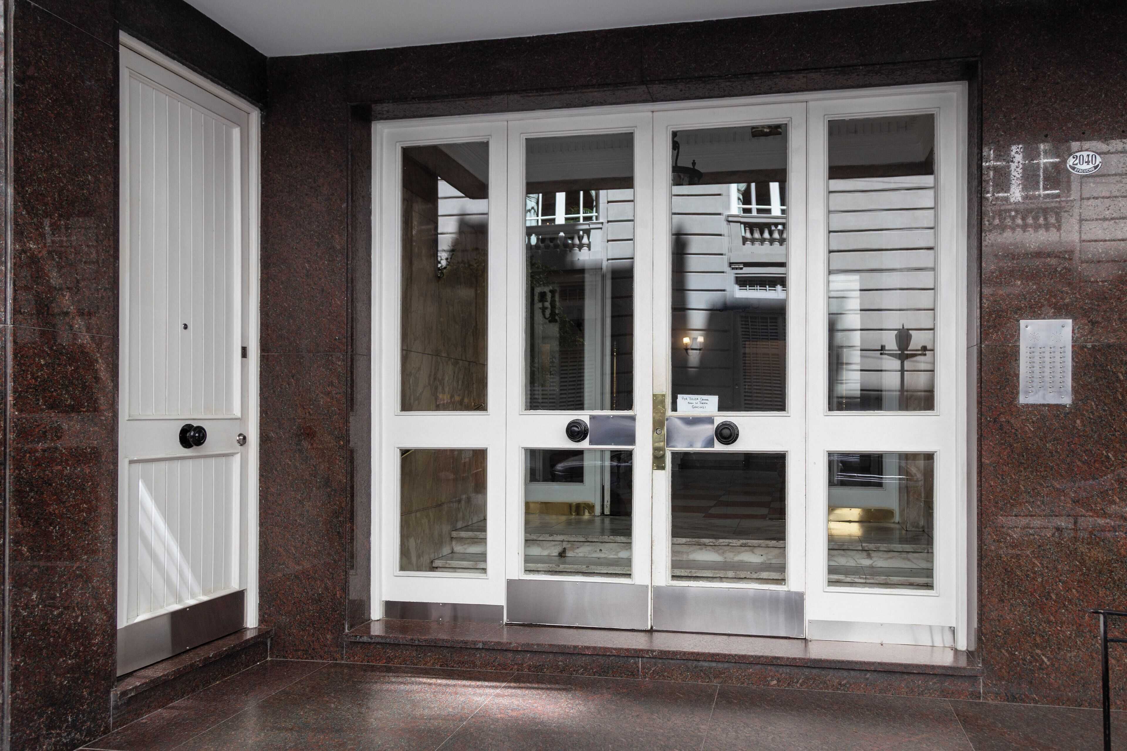 A set of double doors with glass panels, a metal threshold, and a marble wall.